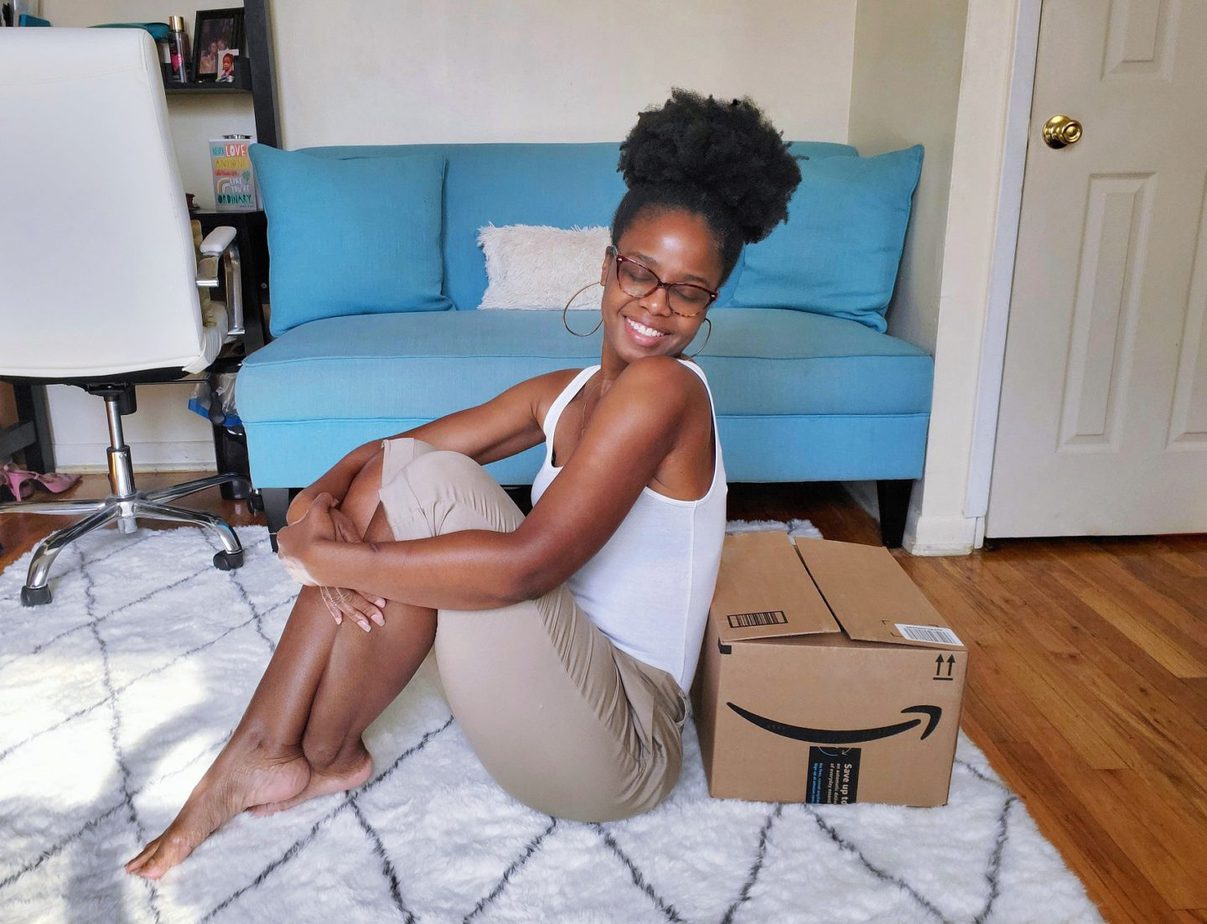 Black woman leaning on Amazon box in living room