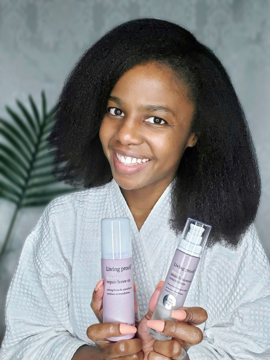 woman with 4c kinky hair blown out holding Living Proof hair products used