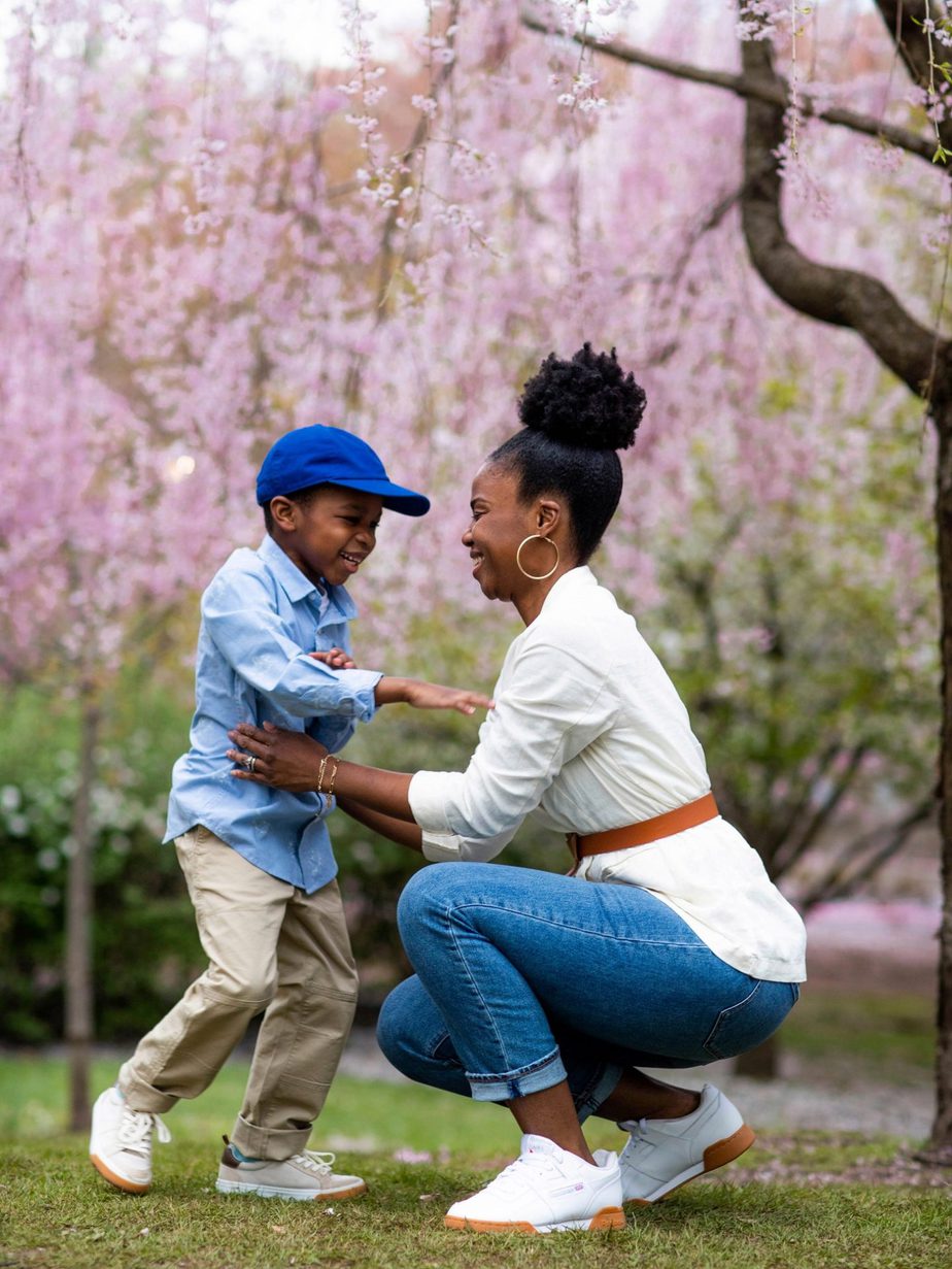 Black mom and little boy hug in park with cherry blossoms